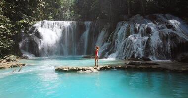 Traveller woman on cascade waterfalls with clear water in Sulawesi. Scenic waterfall in Luwuk, video