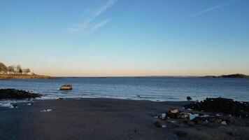 A tranquil coastal view at sunset, featuring a sandy beach with scattered rocks, calm waters, and distant landmasses. Perfect for nature, travel, and relaxation projects. video