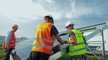 Workers in special uniform installing solar batteries. Men in protective helmets constructing solar panels in a sunny day. Alternative source of energy. video