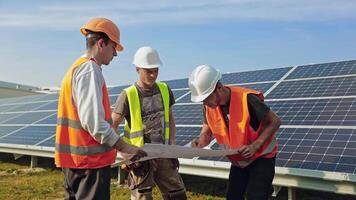 Engineers talking on the solar farm. Group of workers discuss their work while looking at project plan on the sunny batteries background. video