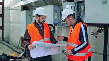 Workers in protective uniform outdoors. Technicians talking about the installation of solar panels on the background of electrical equipment. video