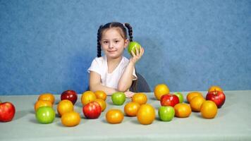 Portrait of a cute little girl with fruits indoors. Ripe fruit on the table. Beautiful smiling child playing with fresh apples on the table. video