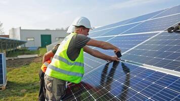 Installation photovoltaic solar panels. Worker fixing solar panel to a metal basis with a drill in a sunny day. Concept of ecological renewable energy. video