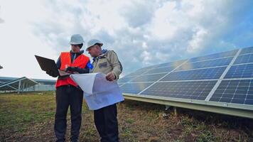 Men in helmets talking about solar panels. Managers discussing the plan on the field with solar panels using a computer laptop. video