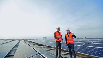 Solar generation technologies. Engineers standing on a flat roof with many solar panels. Workers in protective outfit and hard hats are talking on a modern solar farm. video
