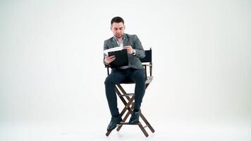Elegant man with a folder. Businessman sitting on the chair and reading documents. Many papers are flying in the studio over the handsome man. video