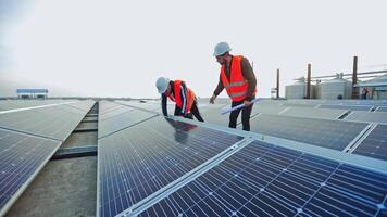 Enginneers installing new sunny batteries. Two workers in a uniform and hardhat installing photovoltaic panels on a solar farm. video