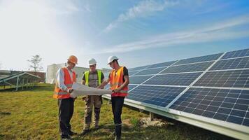 Technicians near the sunny battery in a sunny day. Three workers in protective helmet studying the plan of solar farm. video
