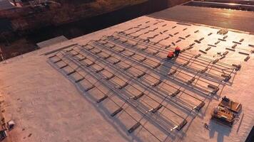Installation solar farm on a roof at sunset. Workers in orange uniform installing metal basis on the roof for solar panels. Aerial view. video