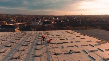 Installation solar panels at sunset. Workers in protective uniform making metal constructions on the roof of a building in the setting sun. video