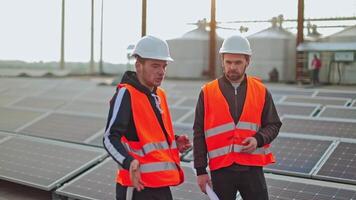 Two engineers in protective uniform on solar farm. Workers in hardhat talking about the installation of sunny panels for renewable energy. video