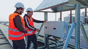 Workers near the modern electricity equipment. Technicians in orange uniform talking about the installation on the solar panels background. video