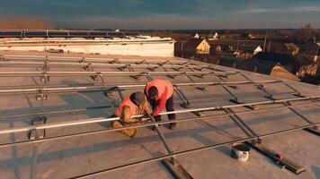 Preparative process for solar energy farm on a building. Workers install metal constructions on roof at sunset. Motion camera around. video