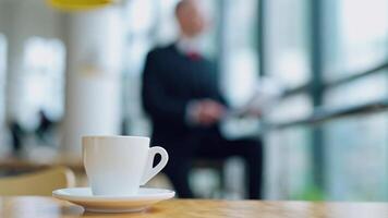 Coffee cup standing on the office desk in front view with a blurred image of businessman working on background. Morning coffe in office. video