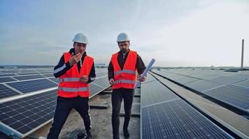 Solar panels for a renewable energy. Workers in protective orange uniform talking on the big power station with solar panels. video