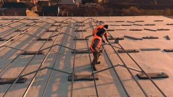 Two workers install metal basis on roof. Technicians in protective uniform prepare place for solar panels. Slow motion. Camera moves around. video