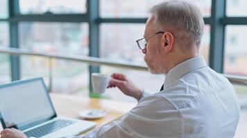 Businessman is checking presentation on a laptop while sitting at a table in light room with panoramic business view. Business . video