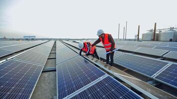 Solar panels installation. Two workers in a uniform and hard hat install photovoltaic panels on a solar farm. Innovative electricity system. video
