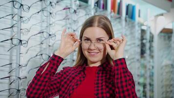 Portrait of a happy woman trying on trendy eyeglasses. Smiling female buyer choosing new glasses and posing on camera in optic store. video