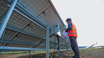 Installing solar panel. Man technician in special uniform connects the photovoltaic panel. View from below on a sunny battery. video