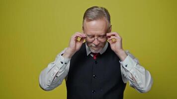 Portrait of a handsome grey-haired man. Mature man taking off his eyeglasses with a smile and looking at camera on yellow background. video