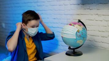 Boy looking at globe learning about virus spreading around the world. Child with curious face thinking about the planet during covid lock down. Concept of COVID-19 pandemic infection. video