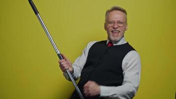 Funny elderly man dancing with a mop. Amusing old man in suit singing happily with a stick like playing the guitar on yellow background. Positive emotions. video