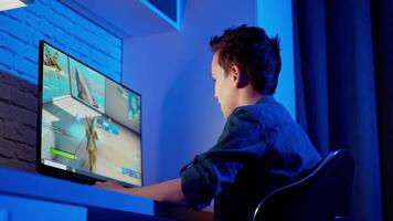 Teen boy plays online game on computer at night. Side view of a gamer playing a game in the room. Teenager becomes angry after losing in computer game. video