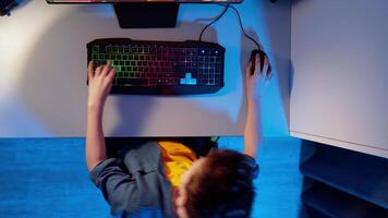 Entertainment at home. View from above on a boy playing on his computer. Teenage boy sitting at the desk and pressing the buttons on a keyboard. Top view. video