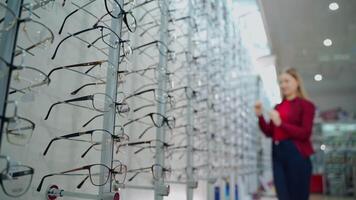 Optical store. Female is choosing eyeglasses. New spectacles arranged on the stands in the eyewear shop. Close-up. video