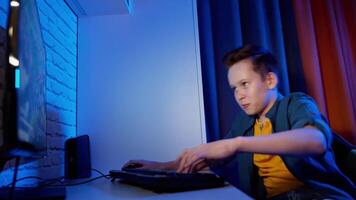 Portrait of teenager playing games. Happy boy sitting in his room and pushing the keyboard buttons while playing on PC. Blue evening light. video