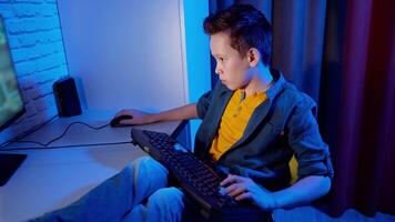 Children's entertainment. Boy is playing games at home. Teenage boy sitting at the desk with a keyboard on legs and concentrated on online games on his computer. video