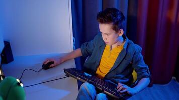 Gamer playing games on a pc at home. Boy is pushing buttons on a keyboard on the desk while playing games in his room. Blue light. video