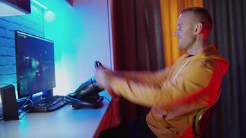 Happy man manages steering wheel in front of computer. Side view of a young man playing games at home. Modern technology. Leisure time concept video