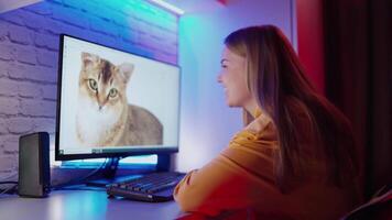 Young girl looking at the screen of a computer. Beautiful woman sitting at the table and touching the monitor with the cat image. video