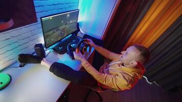 Racing simulator with a steering wheel. Happy young man sits in chair with legs on table playing car racing on the computer. video