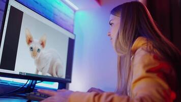 Side view of a woman in front of computer. Happy girl looking at the picture of a funny cat on a screen and admires it. video