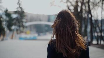 costas Visão do uma mulher caminhando dentro a outono parque com grandes Sombrio cabelo girando costas para a Câmera. seletivo foco usava dentro video