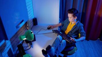 Teen boy is enjoying computer games at home. Boy playing computer games while sitting in the chair with his legs on desk. Top view. video