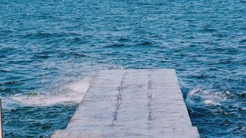 Amazing view from the pier on the sea water. Blue water surface. Waves breaking on the dock in the sea. Slow motion. video