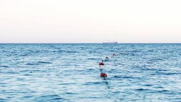 Amazing view of blue sea water with buoys on the rope. Safe swimming zone with markers on the sea. Big ship floating beyond afar. Slow motion. video