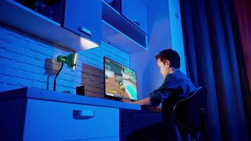 Boy playing game at home. Concentrated gamer sitting at the desk in front of the computer and playing online games. Blue light in the room. video