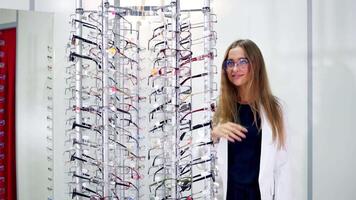 Pretty customer in eyewear store. Lovely girl in eyeglasses standing near the stand with new spectacles and looking at camera. Eyesight concept. video