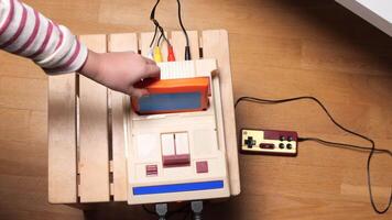Child inserting cartridge into retro game console on wooden table video