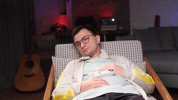 Man sleeping in armchair with remote control after watching tv video