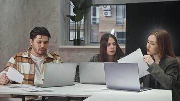Three colleagues are sitting at laptop in office, excitedly discussing project they are working on together. They are sorting out documentation and getting ready to move forward. video