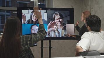 A group of office workers are making a call on the television screen, greeting each other with smiles and waves. video