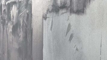 An artist skillfully applies black and white paint to a large canvas, creating an abstract mural in an urban environment under bright daylight video