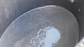 A person is filling a large container with water using a blue tap in a rural location under bright sunlight, showcasing daily water collection practices video