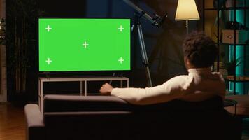 Man using isolated screen smart TV to watch news program broadcasting in living room. Cord cutter watching chroma key ultrawide television display showing VOD channel, relaxing on couch photo